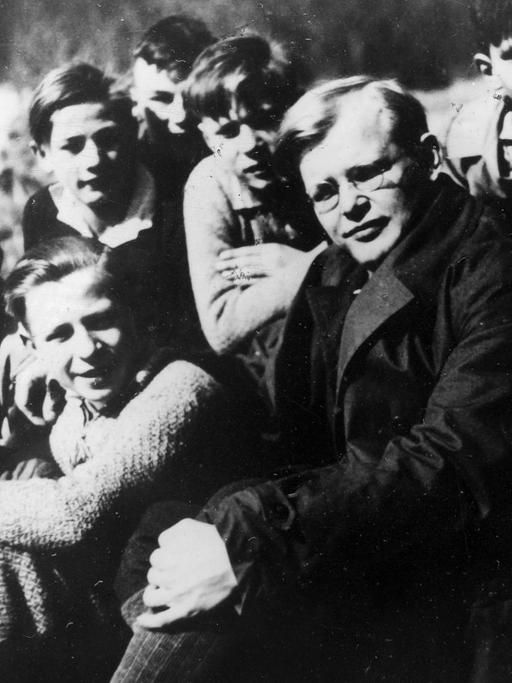 Dietrich Bonhoeffer sitzt inmitten einer Gruppe Jungen an einem Flussufer, alle schauen in die Kamera.