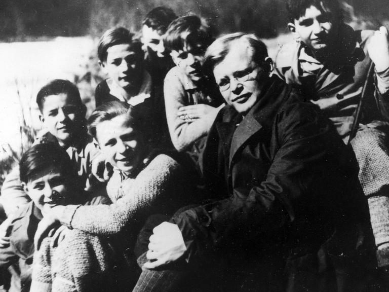 Dietrich Bonhoeffer sitzt inmitten einer Gruppe Jungen an einem Flussufer, alle schauen in die Kamera.