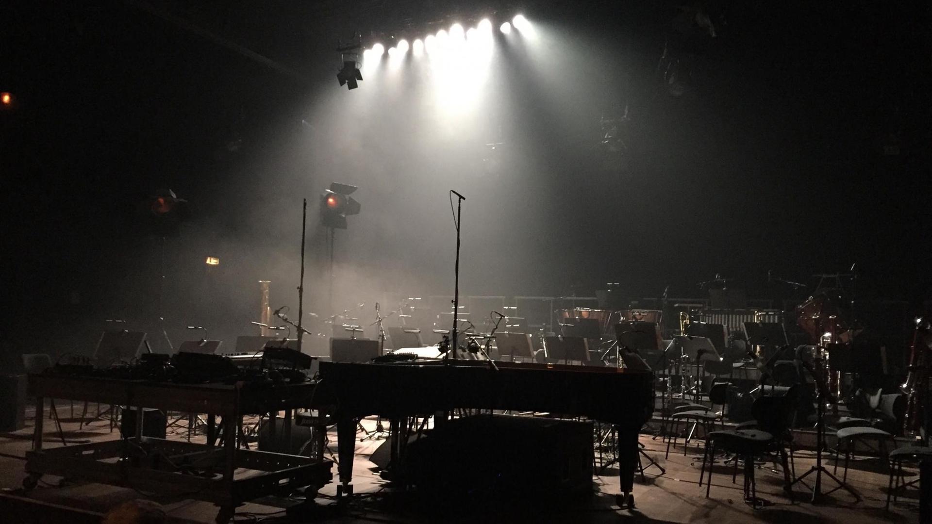 Ein Orchsteraufbau auf einer menschenleeren Bühne im Scheinwerferlicht. Stühle, ein Konzertflügel und andere Instrumente stehen bereit für ein Konzert. Ein Orchsteraufbau auf einer menschenleeren Bühne im Scheinwerferlicht. Stühle, ein Konzertflügel und andere Instrumente stehen bereit für ein Konzert.