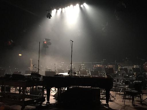 Ein Orchsteraufbau auf einer menschenleeren Bühne im Scheinwerferlicht. Stühle, ein Konzertflügel und andere Instrumente stehen bereit für ein Konzert.