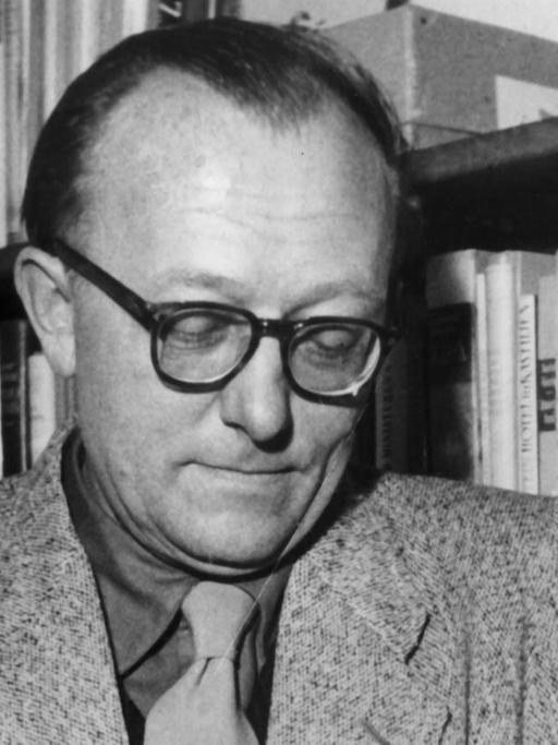 Der deutsche Schriftsteller Günter Eich lehnt an einem Regal und blättert in einem Buch. Aufnahme von 1953.