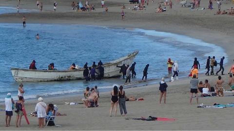 Flüchtlinge landen im Dezember in einem Boot am Strand von Los Cristianos auf der spanischen Insel Teneriffa. Dazwischen sind Touristen.