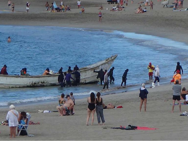 Flüchtlinge landen im Dezember in einem Boot am Strand von Los Cristianos auf der spanischen Insel Teneriffa. Dazwischen sind Touristen.