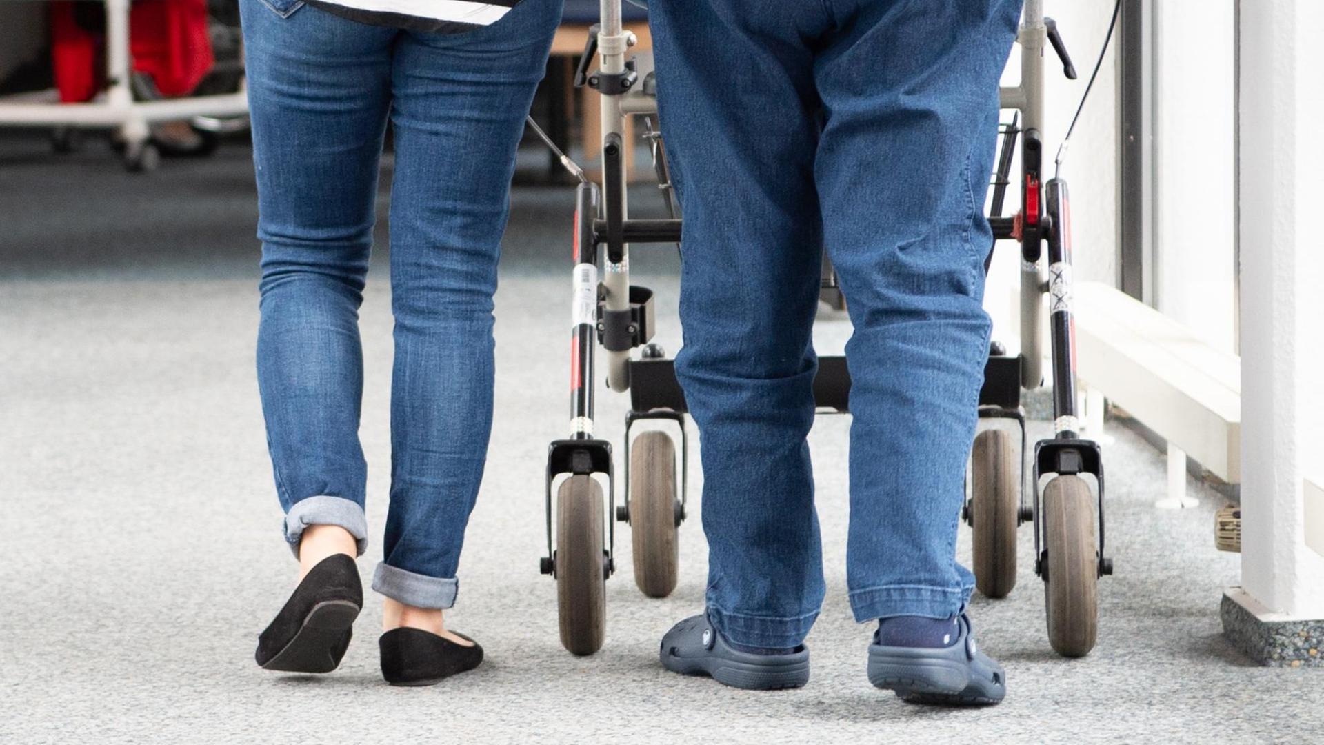 Es sind die Beine eines älteren Menschen, der einen Rollator schiebt zu sehen. Begleitet wird dieser Mensch von einer anderen Person. Es sind die Beine eines älteren Menschen, der einen Rollator schiebt zu sehen. Begleitet wird dieser Mensch von einer anderen Person.