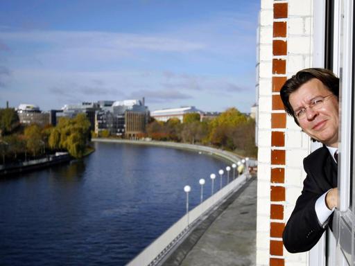 Hans Joachim Mendig, Geschäftsführer von HessenFilm, lent sich in Berlin aus einem Fenster, im Hintergrund ist die Spree zu sehen