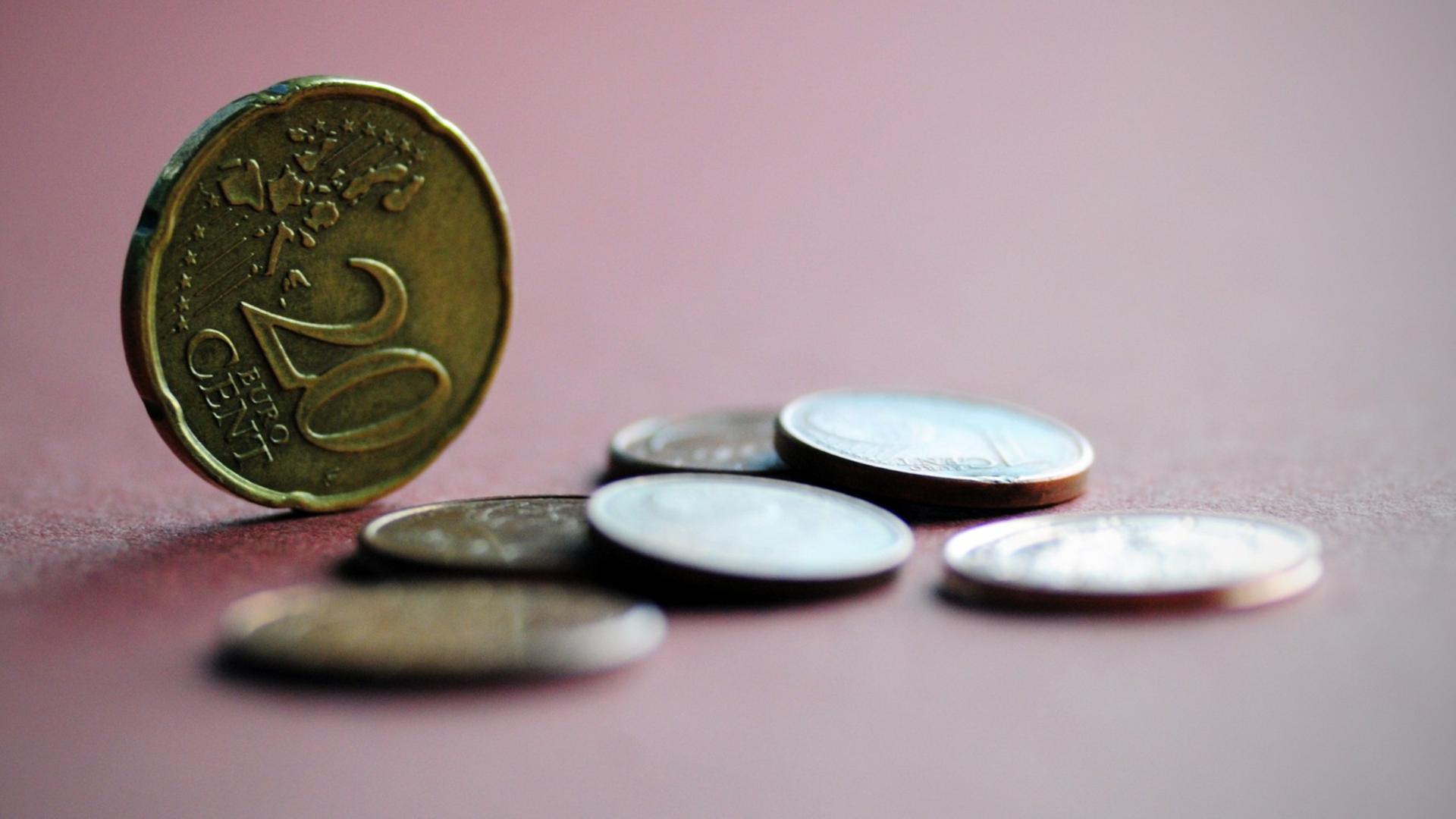 Mehrere Euro-Münzen liegen auf einem farbigen Papier, eine 20-Cent-Münze steht aufrecht