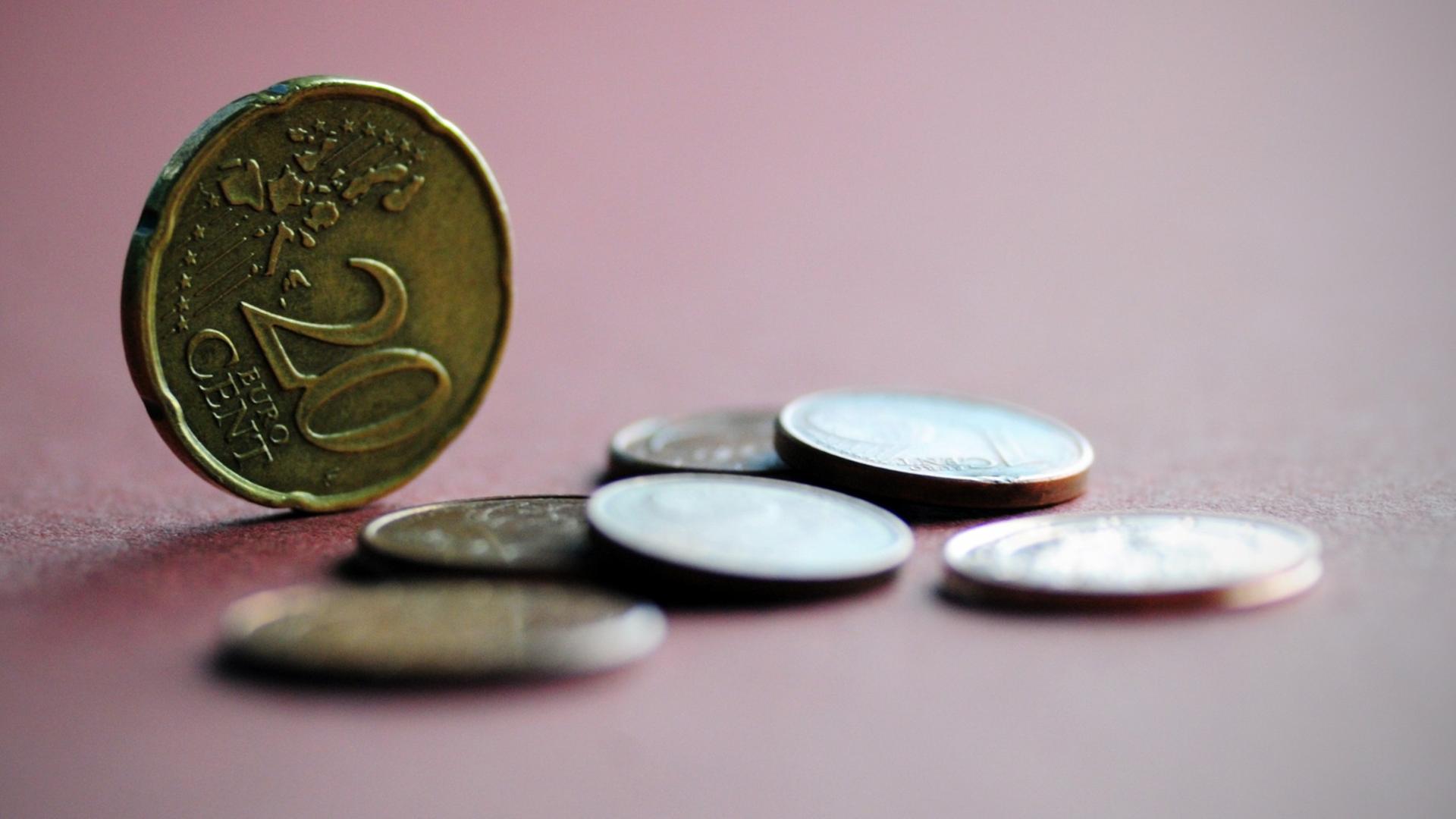 Mehrere Euro-Münzen liegen auf einem farbigen Papier, eine 20-Cent-Münze steht aufrecht Mehrere Euro-Münzen liegen auf einem farbigen Papier, eine 20-Cent-Münze steht aufrecht