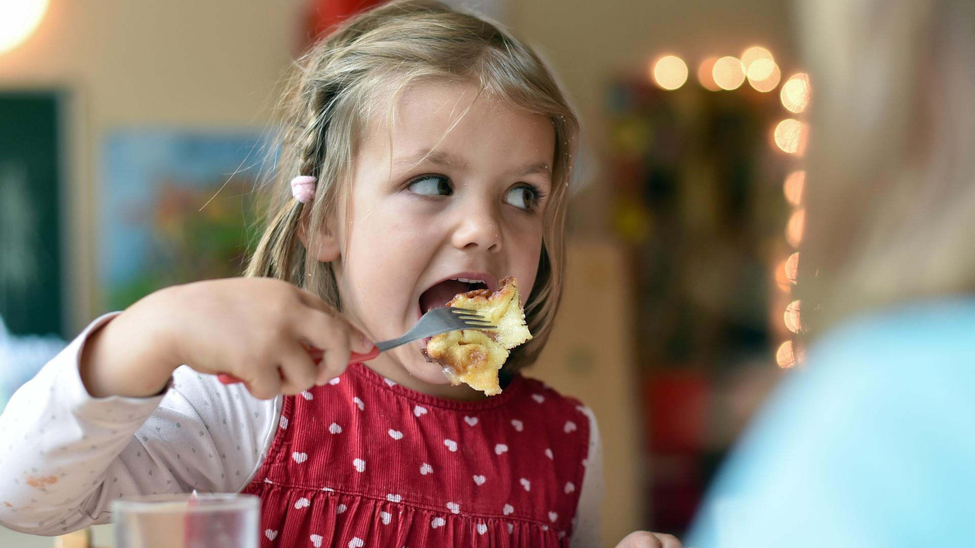 Ein Mädchen isst im Kindergarten Kaiserschmarrn mit Apfelmus und Zimt und Zucker.