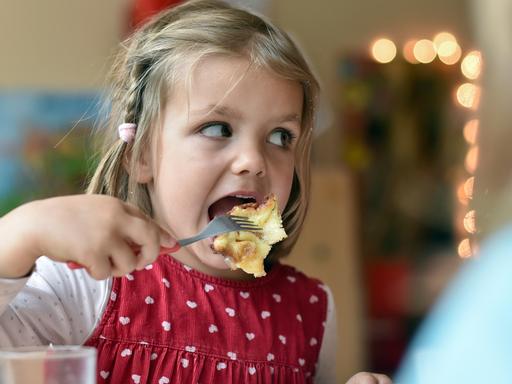 Ein Mädchen isst im Kindergarten Kaiserschmarrn mit Apfelmus und Zimt und Zucker.
