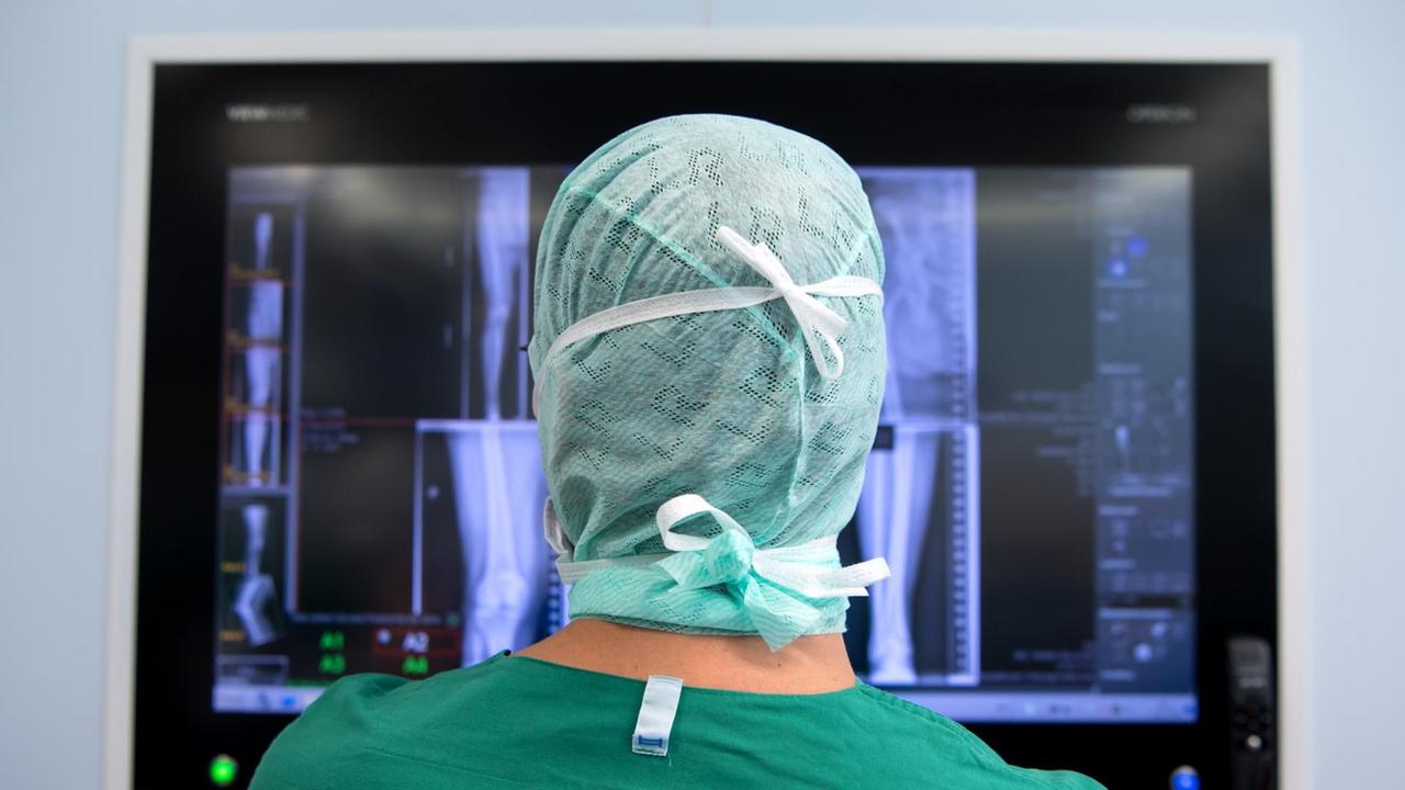 Ein Arzt schaut sich nach einer Knie-Operation in einem Operationssaal Röntgenbilder auf einem Monitor an. Ein Arzt schaut sich nach einer Knie-Operation in einem Operationssaal Röntgenbilder auf einem Monitor an.
