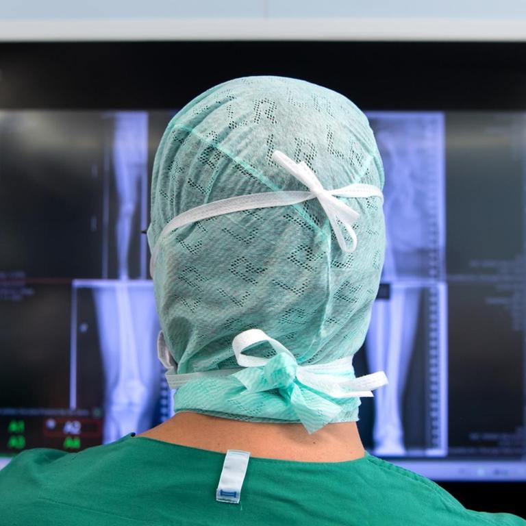 Ein Arzt schaut sich nach einer Knie-Operation in einem Operationssaal Röntgenbilder auf einem Monitor an. 