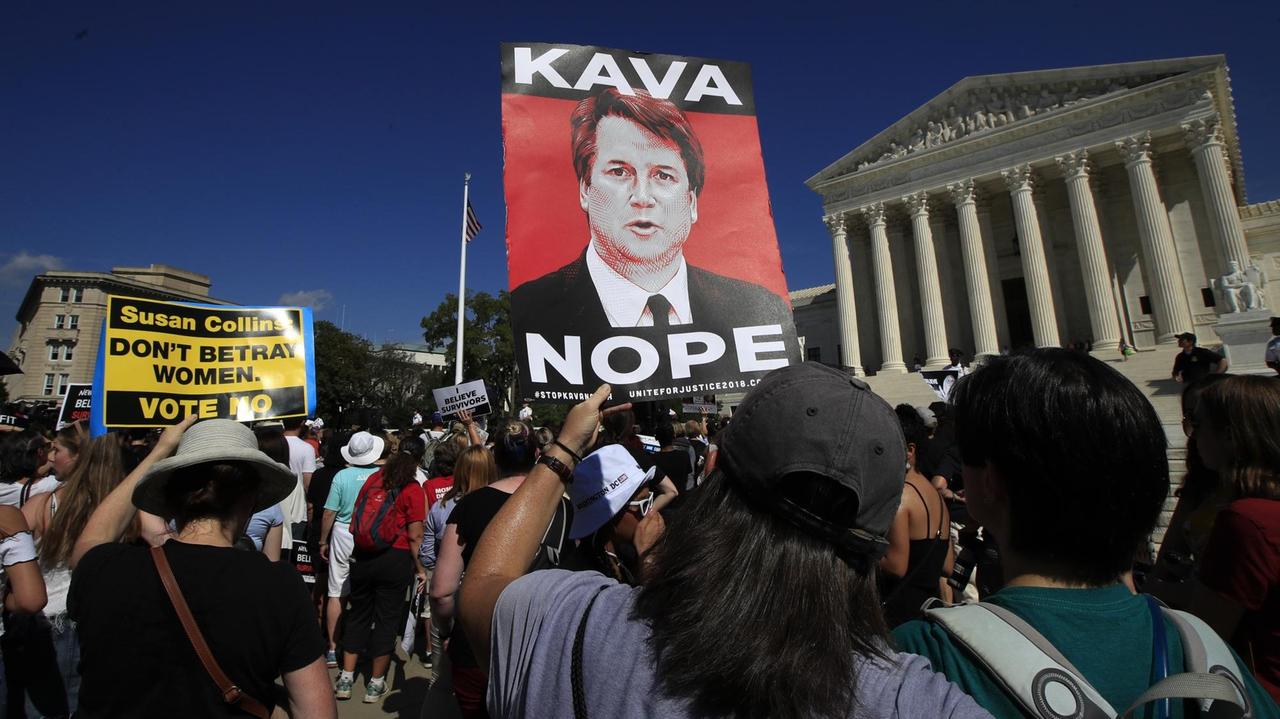 In dem Demonstrationszug hält ein Mann ein Plakat mit dem Kopf Kavanaughs und der Aufschrift "Kava - Nope" in der Hand. Im Hintergrund sieht man das Kapitol. In dem Demonstrationszug hält ein Mann ein Plakat mit dem Kopf Kavanaughs und der Aufschrift "Kava - Nope" in der Hand. Im Hintergrund sieht man das Kapitol.