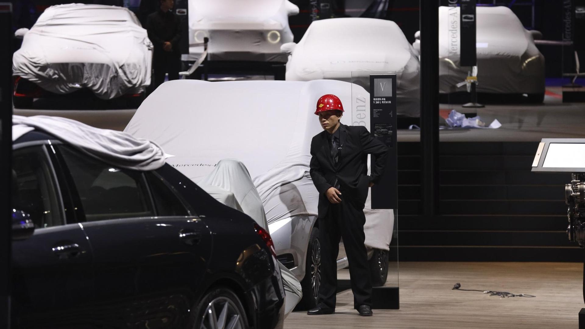 15.04.2019, China, Shanghai: Ein Arbeiter steht in der Nähe von gedeckten Fahrzeugen in einer Halle der Auto Shanghai 2019. Foto: Ng Han Guan/AP/dpa +++ dpa-Bildfunk +++ 15.04.2019, China, Shanghai: Ein Arbeiter steht in der Nähe von gedeckten Fahrzeugen in einer Halle der Auto Shanghai 2019. Foto: Ng Han Guan/AP/dpa +++ dpa-Bildfunk +++