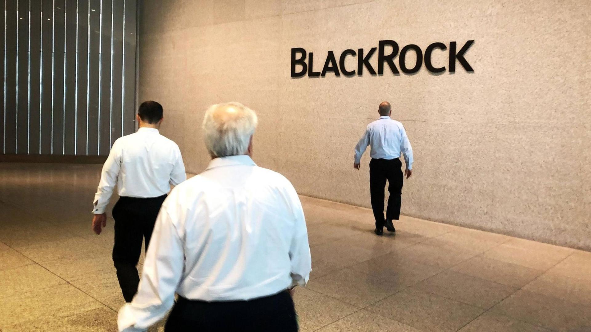 Firmensitz von BlackRock in New York. Drei Männer laufen in einer Halle, im Hintergrund steht an einer Wand BlackRock.