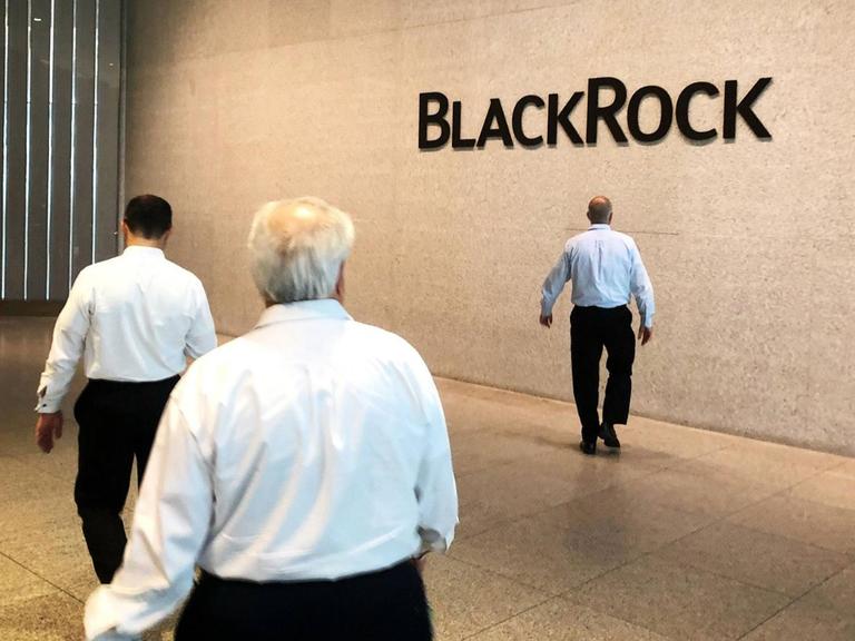 Firmensitz von BlackRock in New York. Drei Männer laufen in einer Halle, im Hintergrund steht an einer Wand BlackRock.