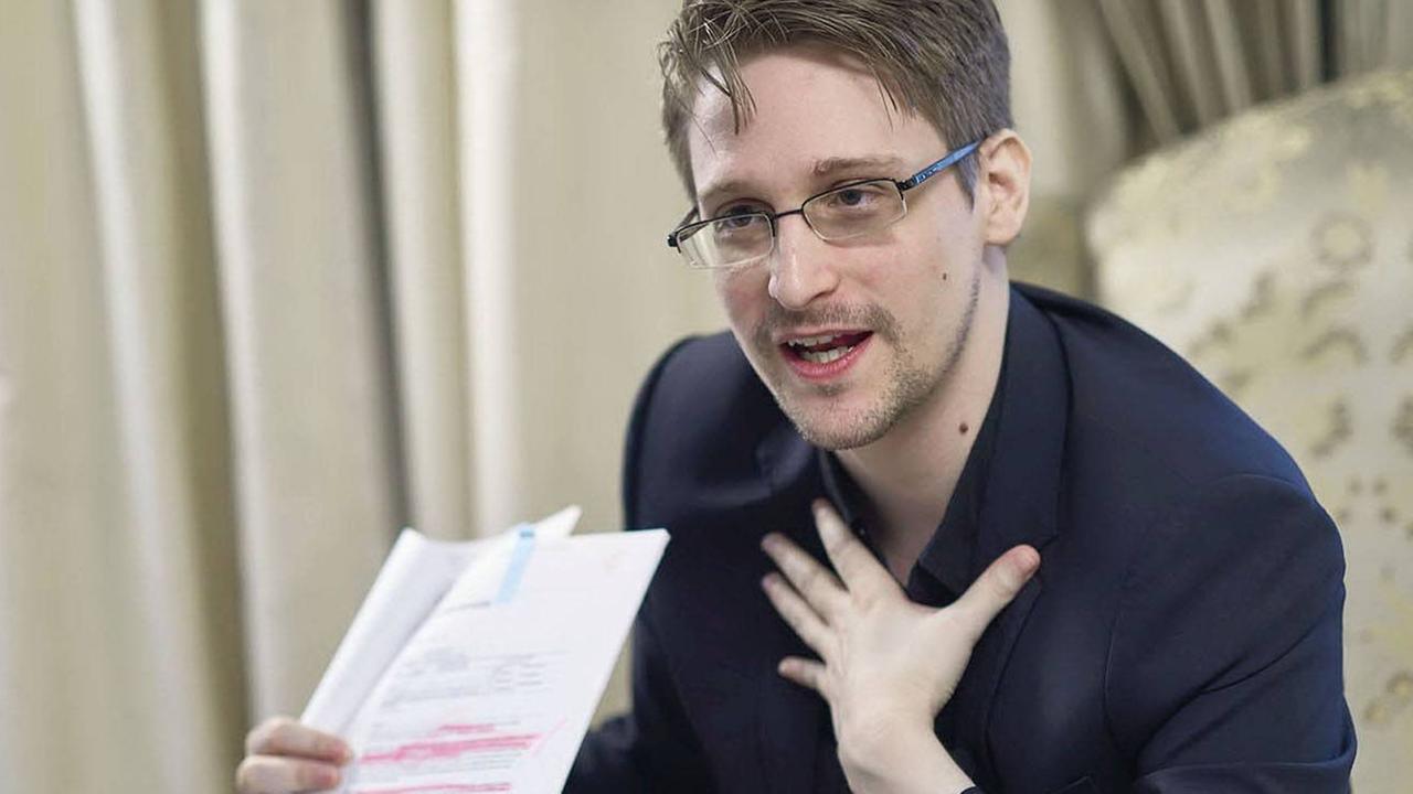 Snowden sitzt auf einem Sessel und zeigt ein Dokument Snowden sitzt auf einem Sessel und zeigt ein Dokument
