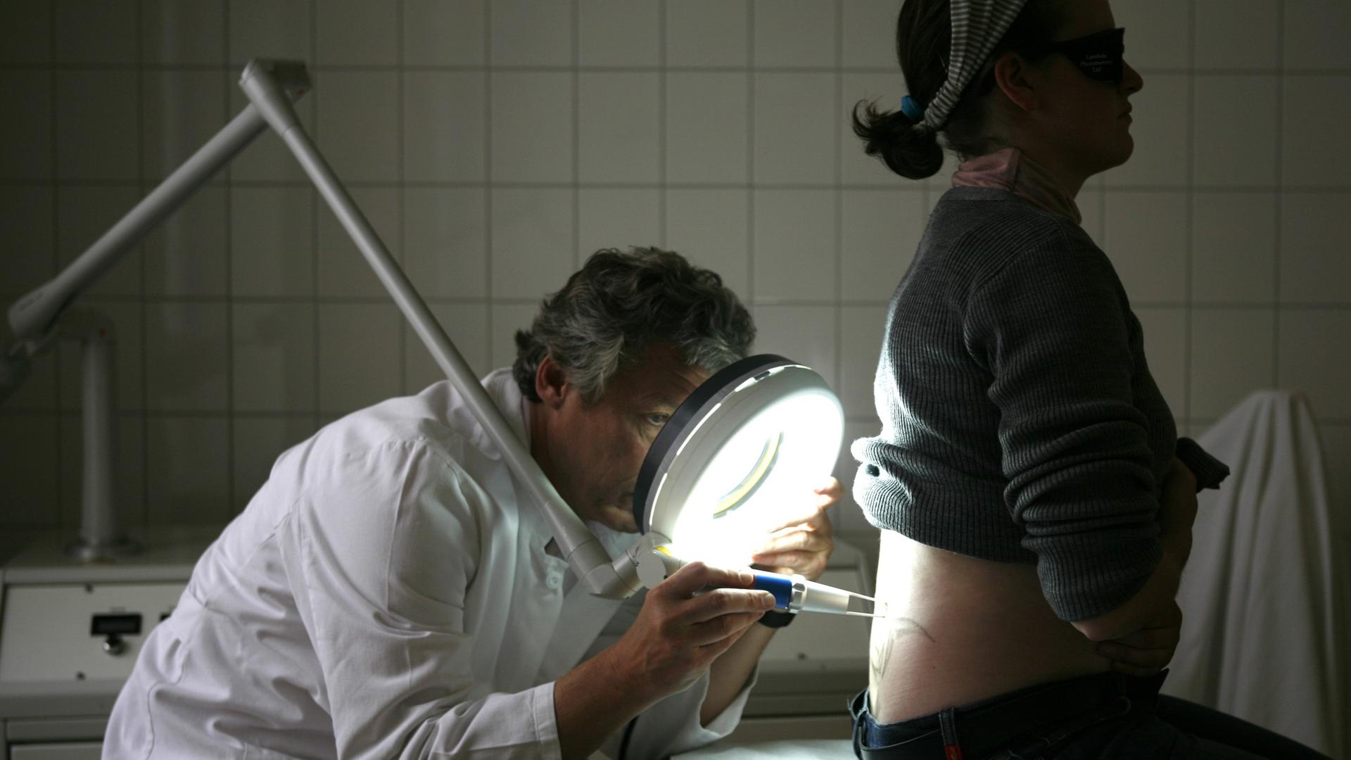 Ein Dermatologe entfernt mit einem Laser die Tätowierung einer Patientin. Ein Dermatologe entfernt mit einem Laser die Tätowierung einer Patientin.