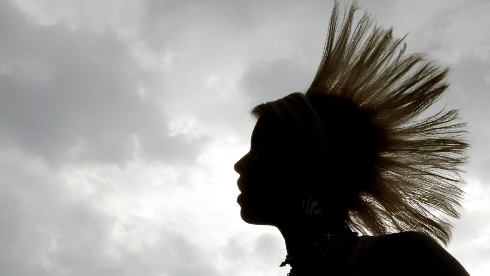 Eine Frau mit Irokesenschnitt im Profil vor grauem Himmel Eine Frau mit Irokesenschnitt im Profil vor grauem Himmel