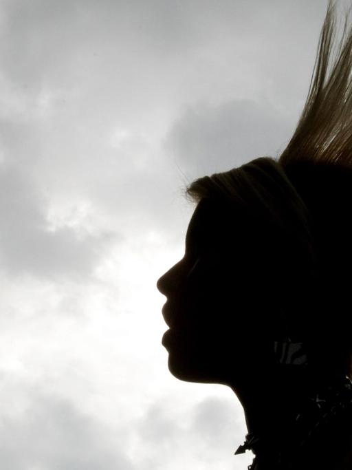 Eine Frau mit Irokesenschnitt im Profil vor grauem Himmel
