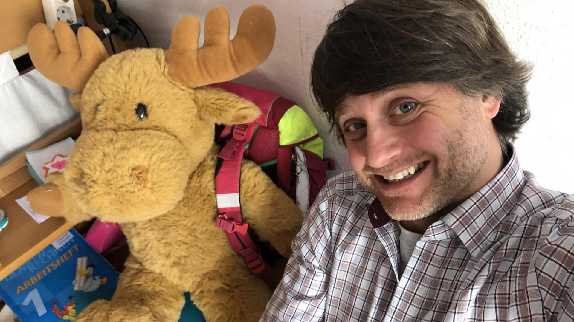 Deutschlandradio-Korrespondent Michael Watzke im Kinderzimmer. Neben ihm sitzt ein Plüschelch.