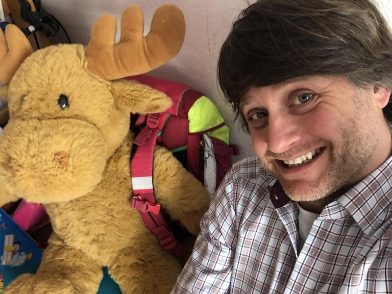 Deutschlandradio-Korrespondent Michael Watzke im Kinderzimmer. Neben ihm sitzt ein Plüschelch.