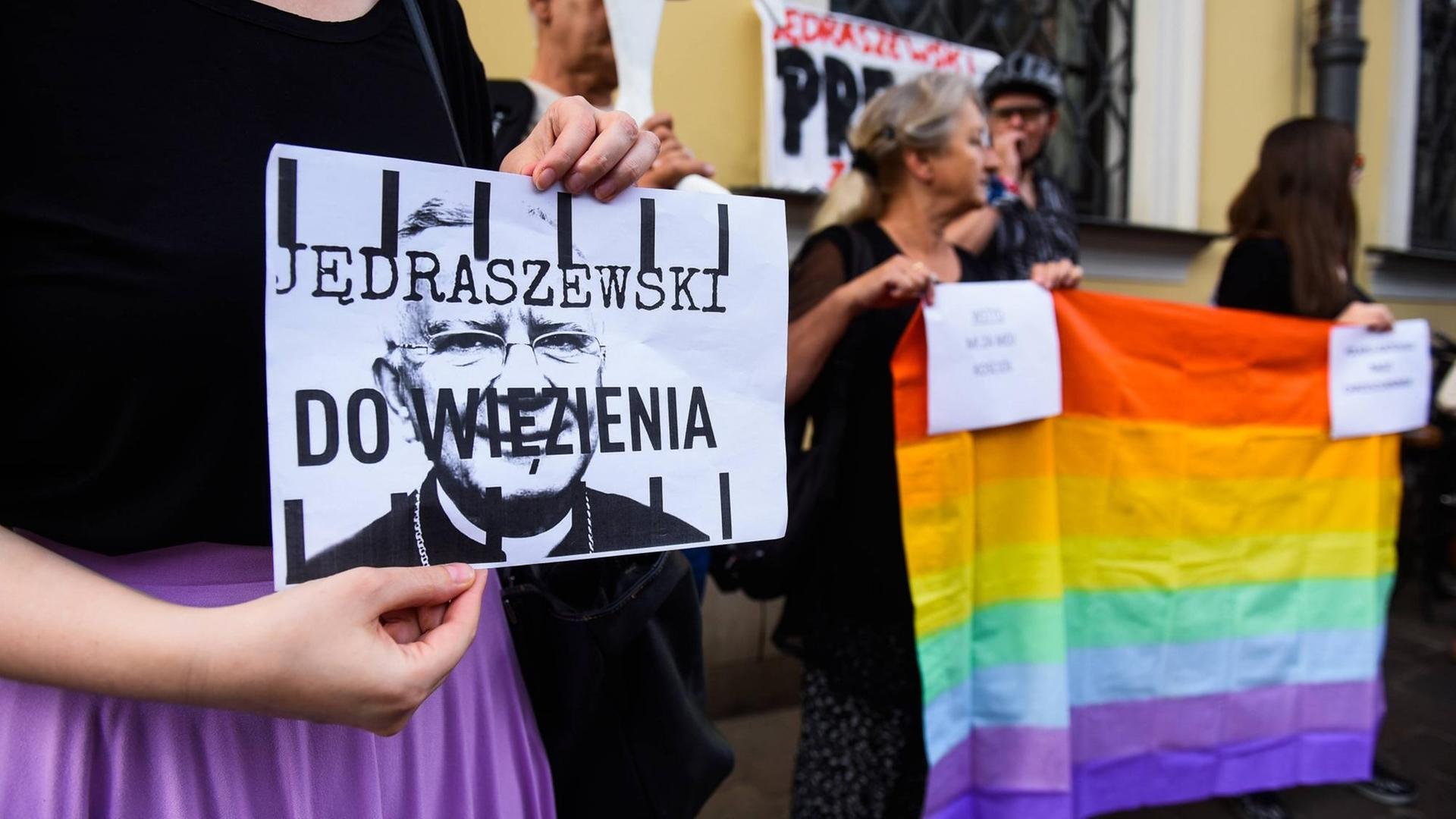 Eine Frau hält bei einer Demonstration in Krakau am 4. August 2019 ein Plakat, auf dem steht: "Jedraszewski ins Gefängnis". Menschen neben ihr halten eine Regenbogenfahne in die Höhe. Der Protest richtet sich gegen den Erzbischof von Krakau, Marek Jedraszewski, der die polnische LGBT-Bewegung mit einer Seuche verglichen hatte.