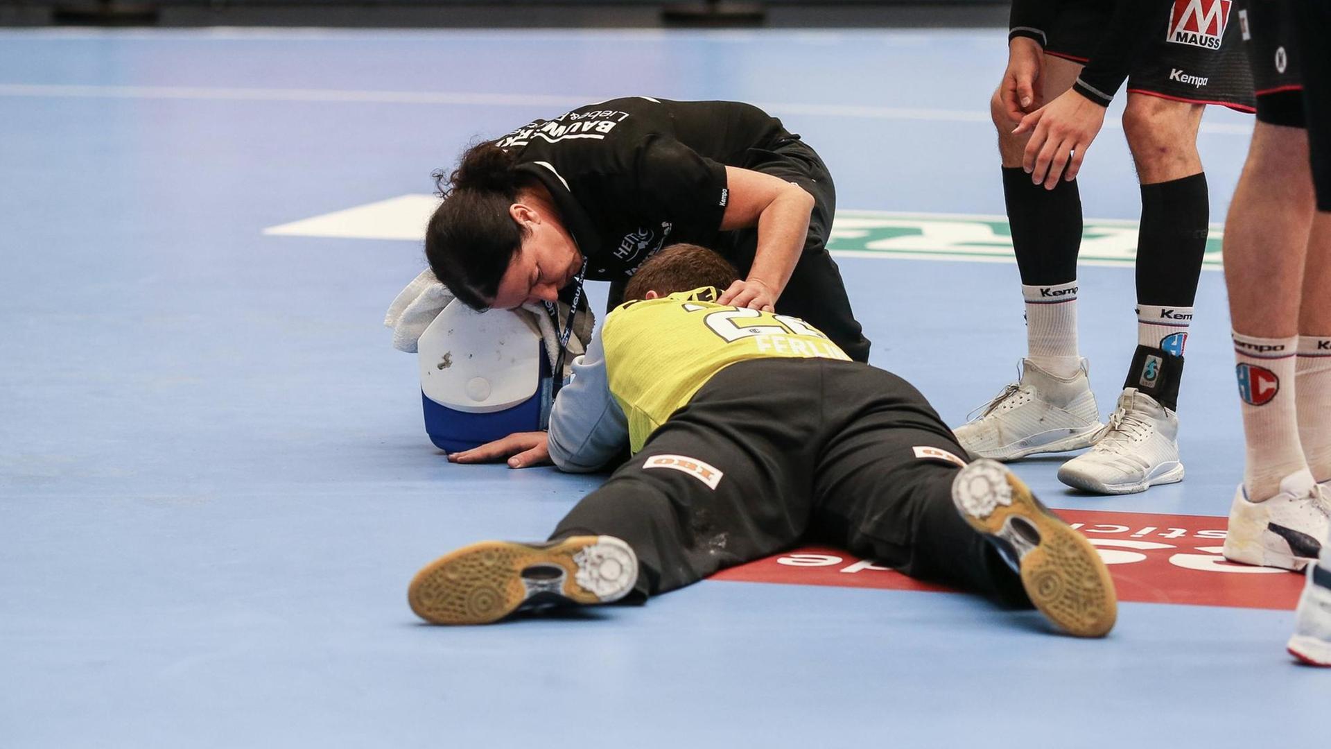 Ein Spieler wird während eines Spiels in der Hanball-Bundesliga auf dem Spielfeld von einem Arzt behandelt. Daneben stehen seine Mitspieler. Ein Spieler wird während eines Spiels in der Hanball-Bundesliga auf dem Spielfeld von einem Arzt behandelt. Daneben stehen seine Mitspieler.