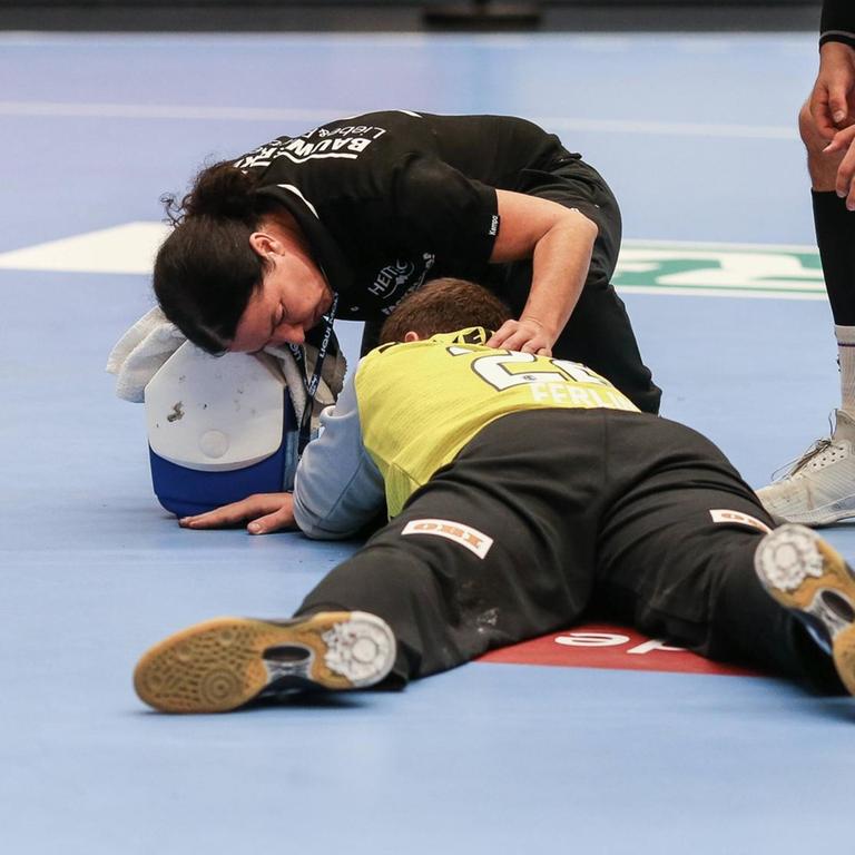 Ein Spieler wird während eines Spiels in der Hanball-Bundesliga auf dem Spielfeld von einem Arzt behandelt. Daneben stehen seine Mitspieler.