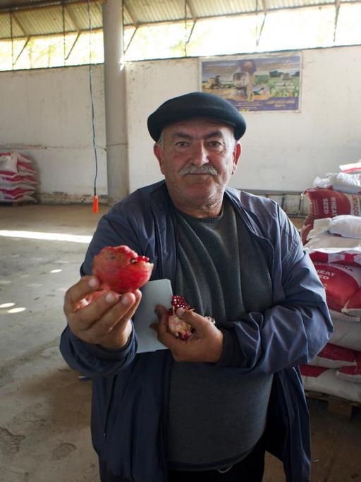 Ein Mann steht in einer Halle und zeigt einen Granatapfel in die Kamera