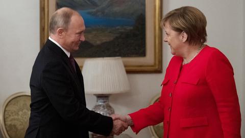 Zu sind Bundeskanzlerin Merkel und Russlands Präsident Putin, die sich begrüßen und die Hand geben.