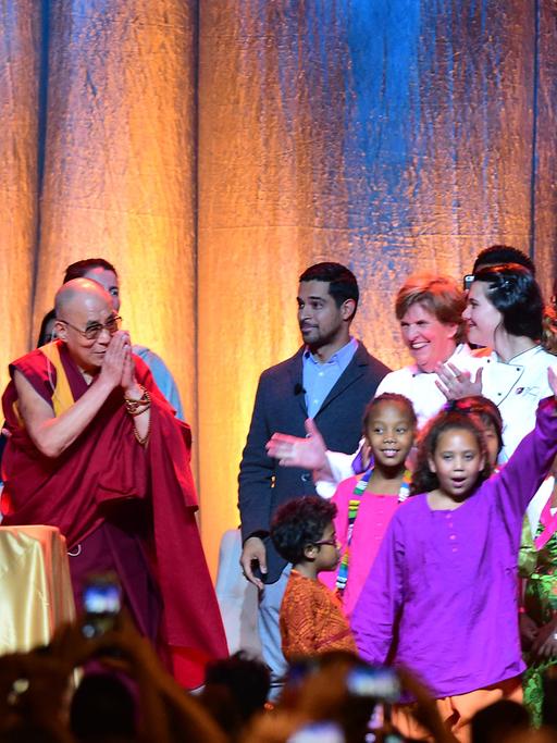 Der Dalai Lama steht auf einer Bühne, neben ihm eine übermannshohe Geburtstagstorte mit einer großen 80., der Musiker Michael Frente Kinder.