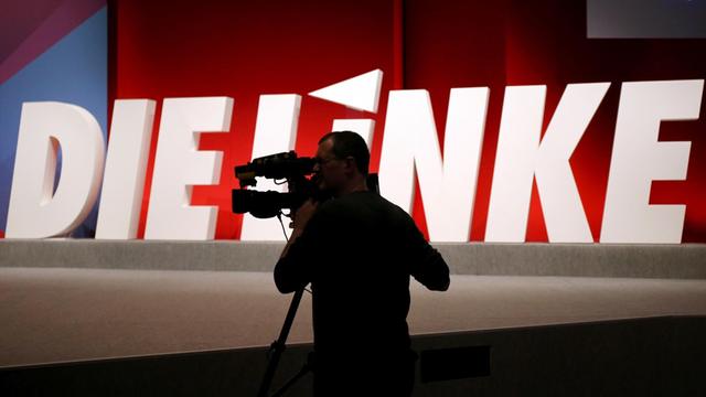 Ein Kameramann steht vor dem Logo der Linkspartei.