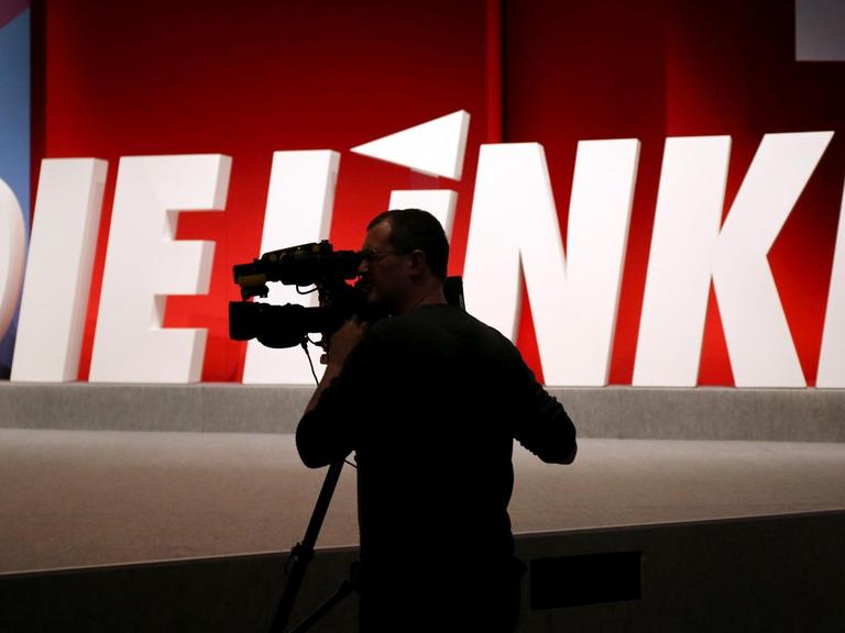Ein Kameramann steht vor dem Logo der Linkspartei.