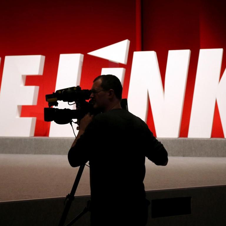 Ein Kameramann steht vor dem Logo der Linkspartei. 
