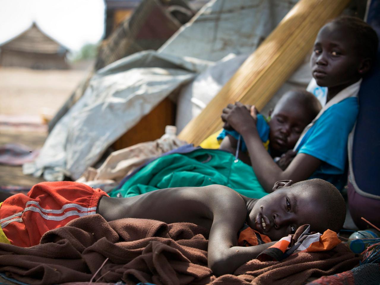 Ein Foto des Kinderhilfswerks UNICEF zeigt drei Kinder in der südsudanesischen Stadt Mingkaman, während sie erschöpft darauf warten, als Hilfesuchende registriert zu werden. Ein Foto des Kinderhilfswerks UNICEF zeigt drei Kinder in der südsudanesischen Stadt Mingkaman, während sie erschöpft darauf warten, als Hilfesuchende registriert zu werden.