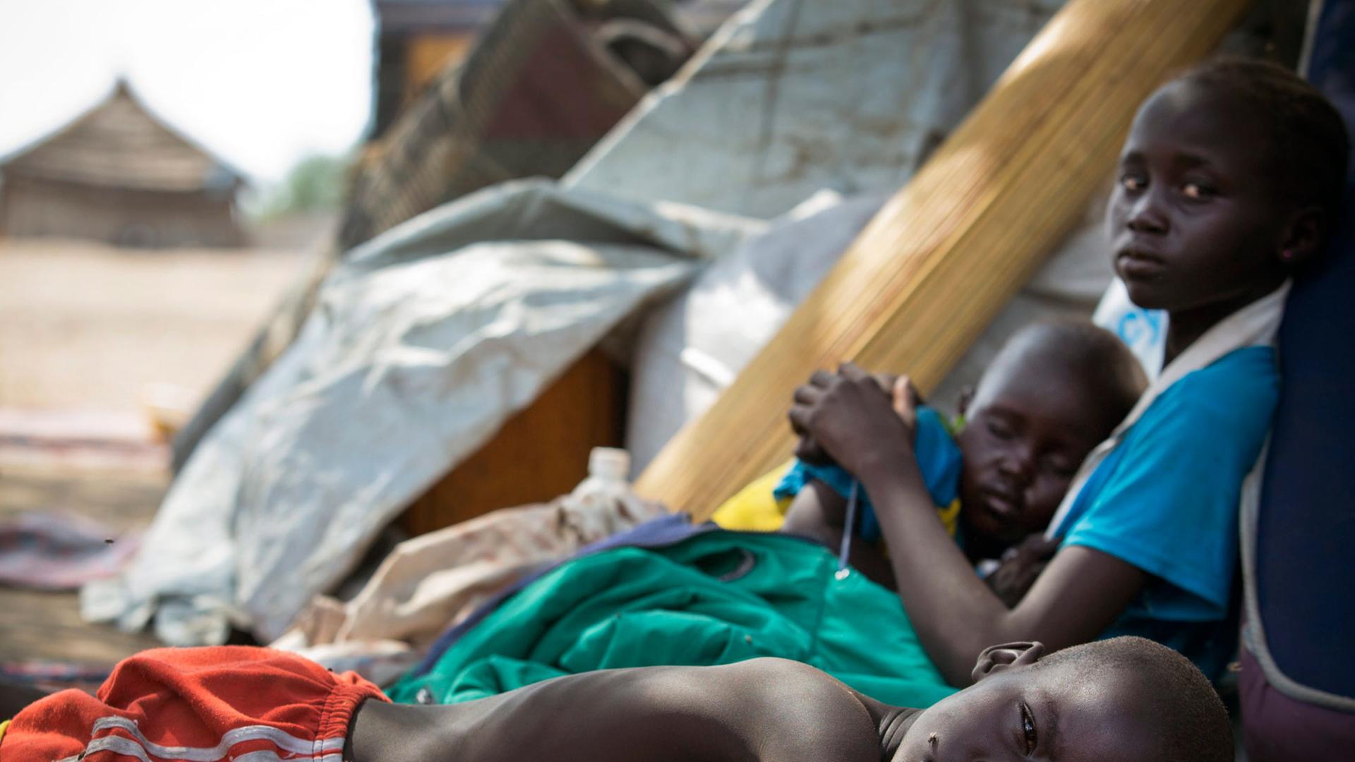 Ein Foto des Kinderhilfswerks UNICEF zeigt drei Kinder in der südsudanesischen Stadt Mingkaman, während sie erschöpft darauf warten, als Hilfesuchende registriert zu werden.
