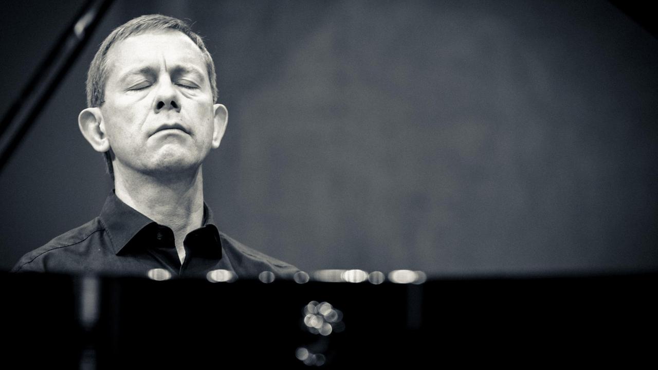 Blick durch den geöffneten Flügel auf das vertiefte Gesicht des Pianisten, der gerade spielt. Blick durch den geöffneten Flügel auf das vertiefte Gesicht des Pianisten, der gerade spielt.