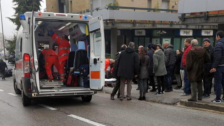 Das Bild zeigt einen Krankenwagen im mittelitalienischen Macerata. Rettungskräfte kümmern sich um einen angeschossenen Mann. Auf einem benachbarten Gehweg sind zuschauende Passanten zu sehen. 