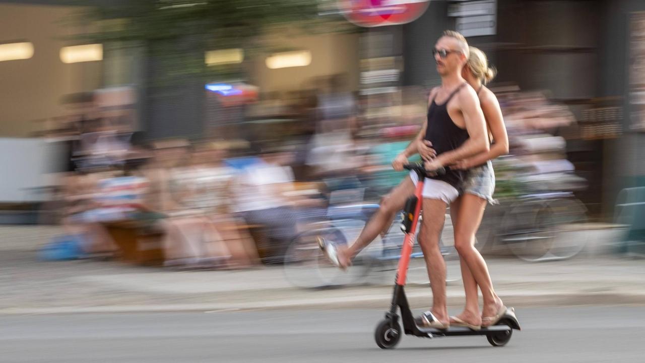 Ein Paar fährt zu zweit fährt mit einem E-Scooter auf der Strasse durch Berlin. Ein Paar fährt zu zweit fährt mit einem E-Scooter auf der Strasse durch Berlin.