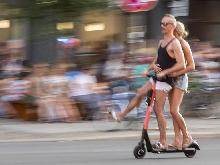Ein Paar fährt zu zweit fährt mit einem E-Scooter auf der Strasse durch Berlin.