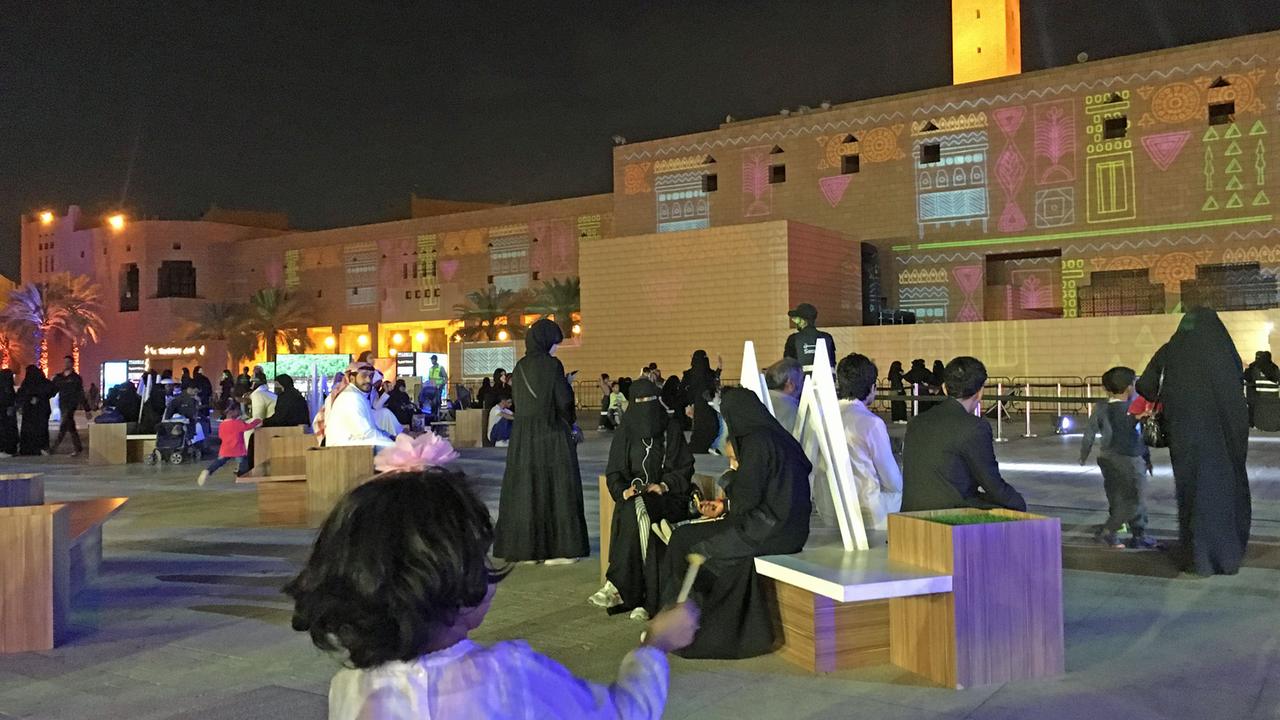 Auf einem Platz in Riad sitzen Männer und Frauen in traditioneller Kleidung auf Bänken. Auf einem Platz in Riad sitzen Männer und Frauen in traditioneller Kleidung auf Bänken.