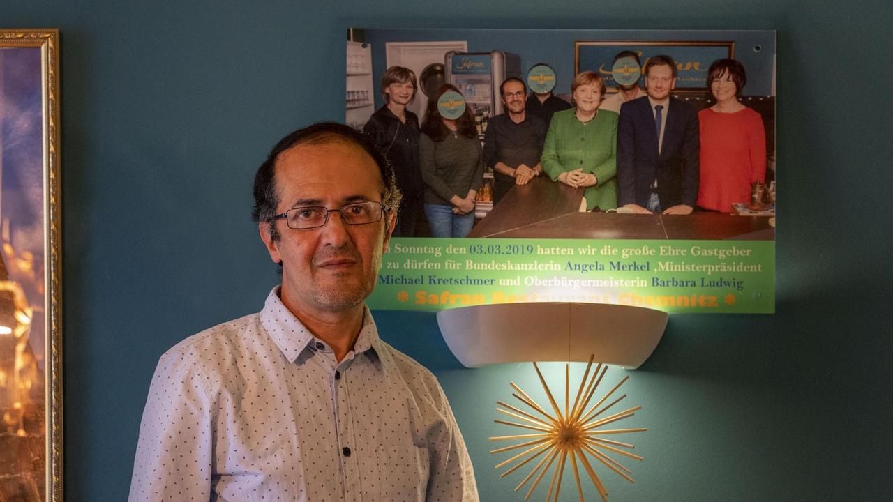 Masoud Hashemi vor einem Foto mit der Bundeskanzlerin und weiteren Personen in seinem Restaurant. Masoud Hashemi vor einem Foto mit der Bundeskanzlerin und weiteren Personen in seinem Restaurant.