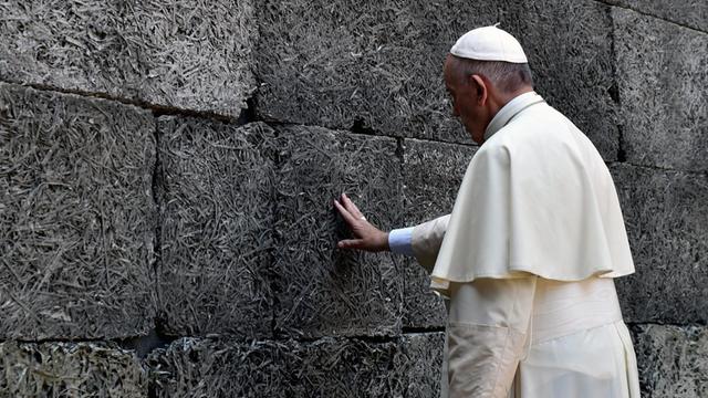 Papst Franziskus berührt mit dem rechten Arm die sogenannte "Schwarze Wand" in Auschwitz.
