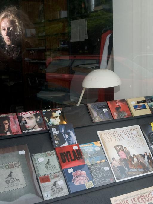 Eine junge Frau blickt auf ihren MP3-Player, während sie vor dem Schaufenster eines Plattenladens steht.