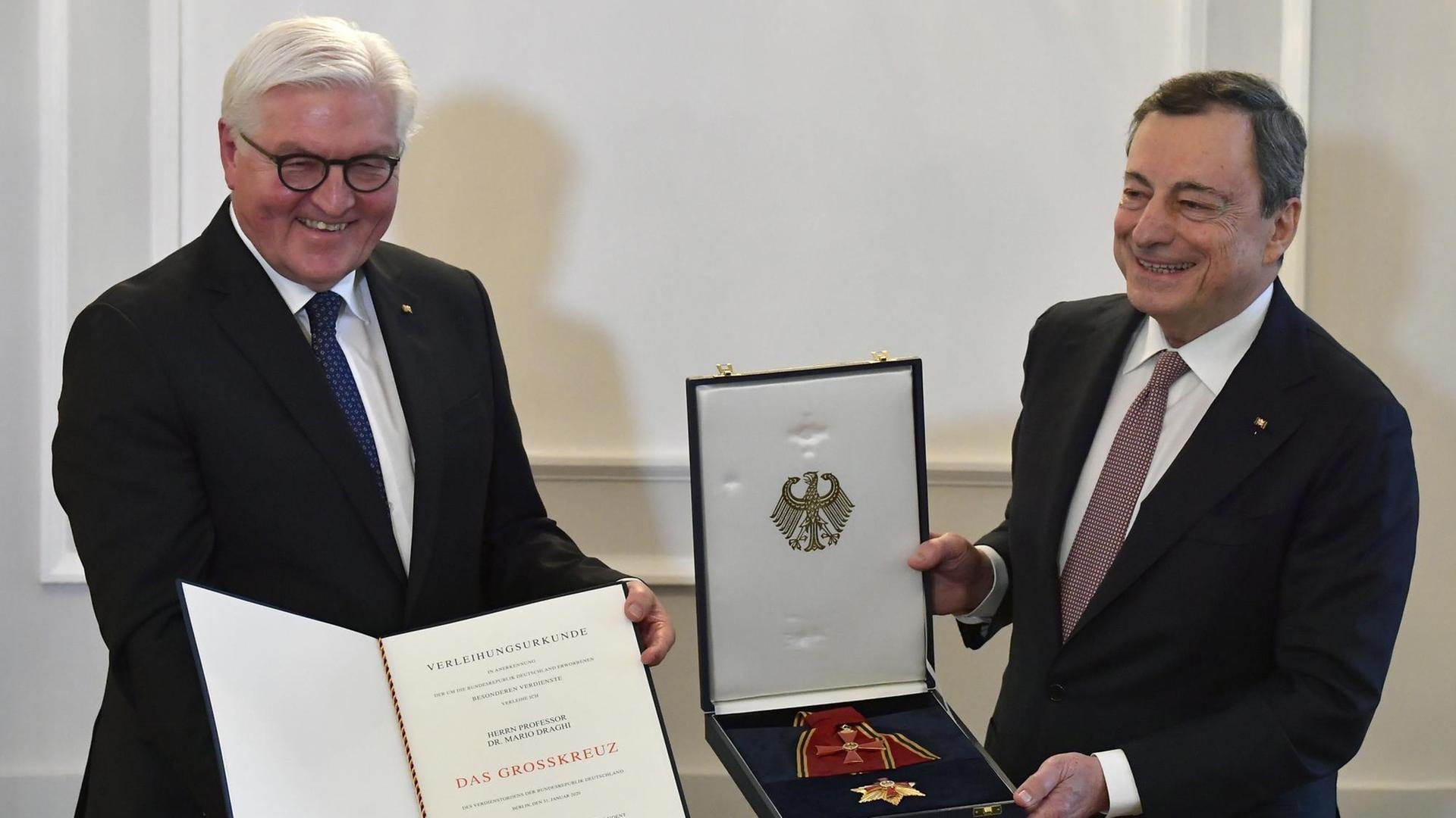 Bundespräsident Steinmeier hält eine Urkunde in der Hand. Ex-EZB-Präsident Draghi zeigt seinen Verdienstorden der Bundesrepublik.