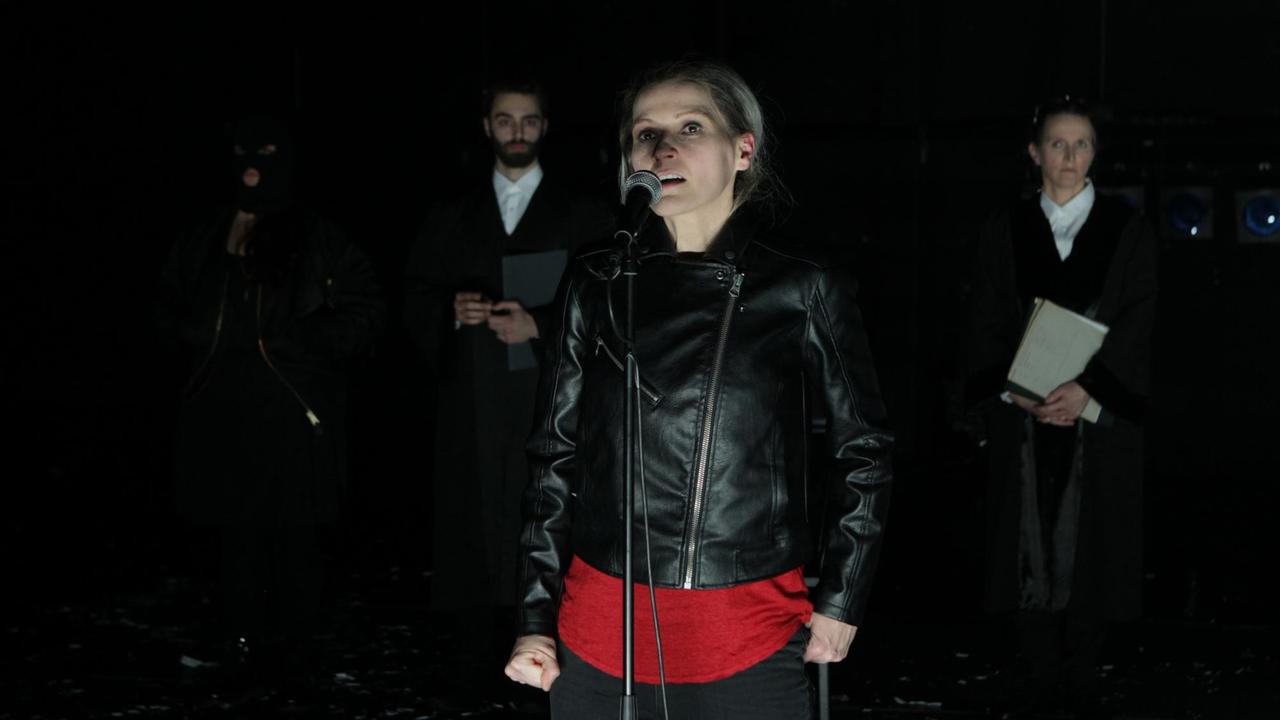 Nadine Geyersbach in "Aus dem Nichts" in der Regie von Nurkan Erpulat nach dem gleichnamigen Film von Fatih Akin. Eine Schauspielerin steht auf einer Bühne vor einem Mikrofon.