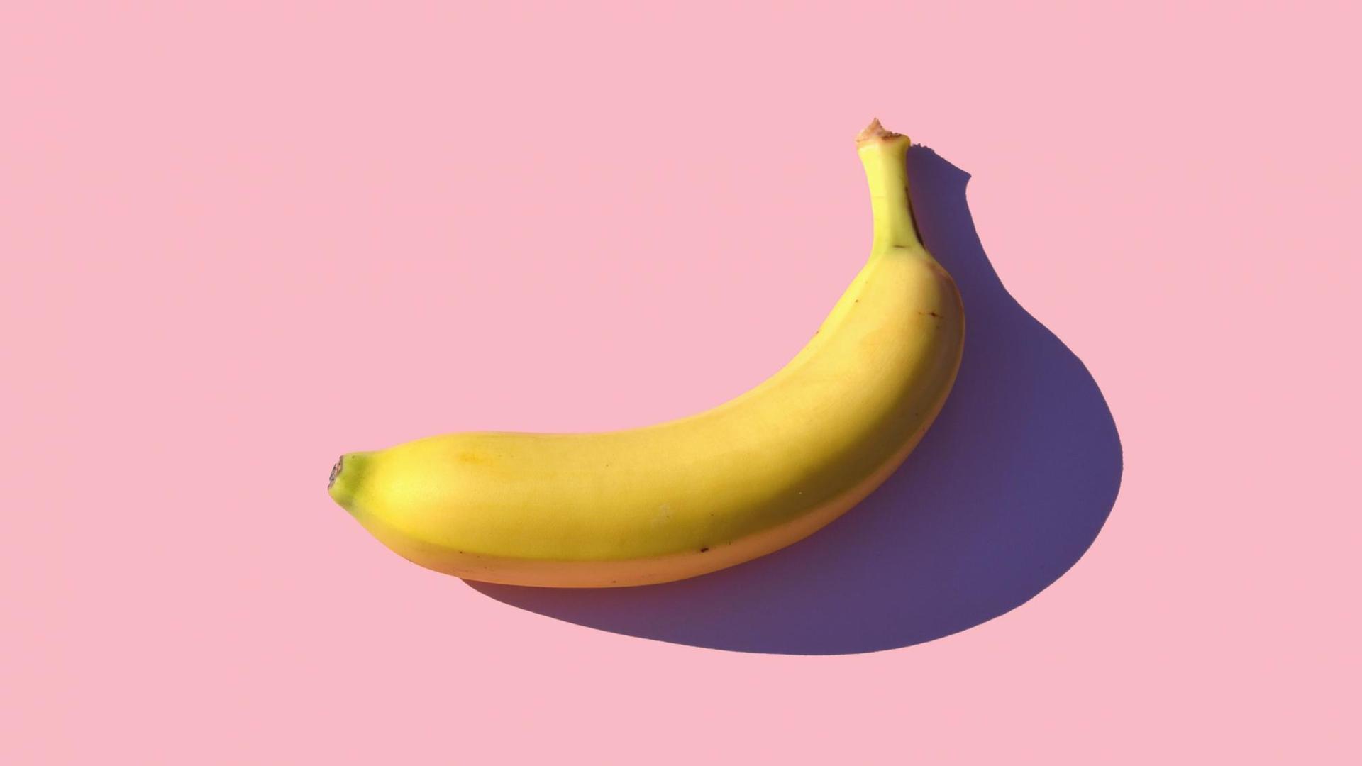 Eine Banane liegt auf einem rosa Untergrund und wirft einen scharfen Schatten darauf. Eine Banane liegt auf einem rosa Untergrund und wirft einen scharfen Schatten darauf.