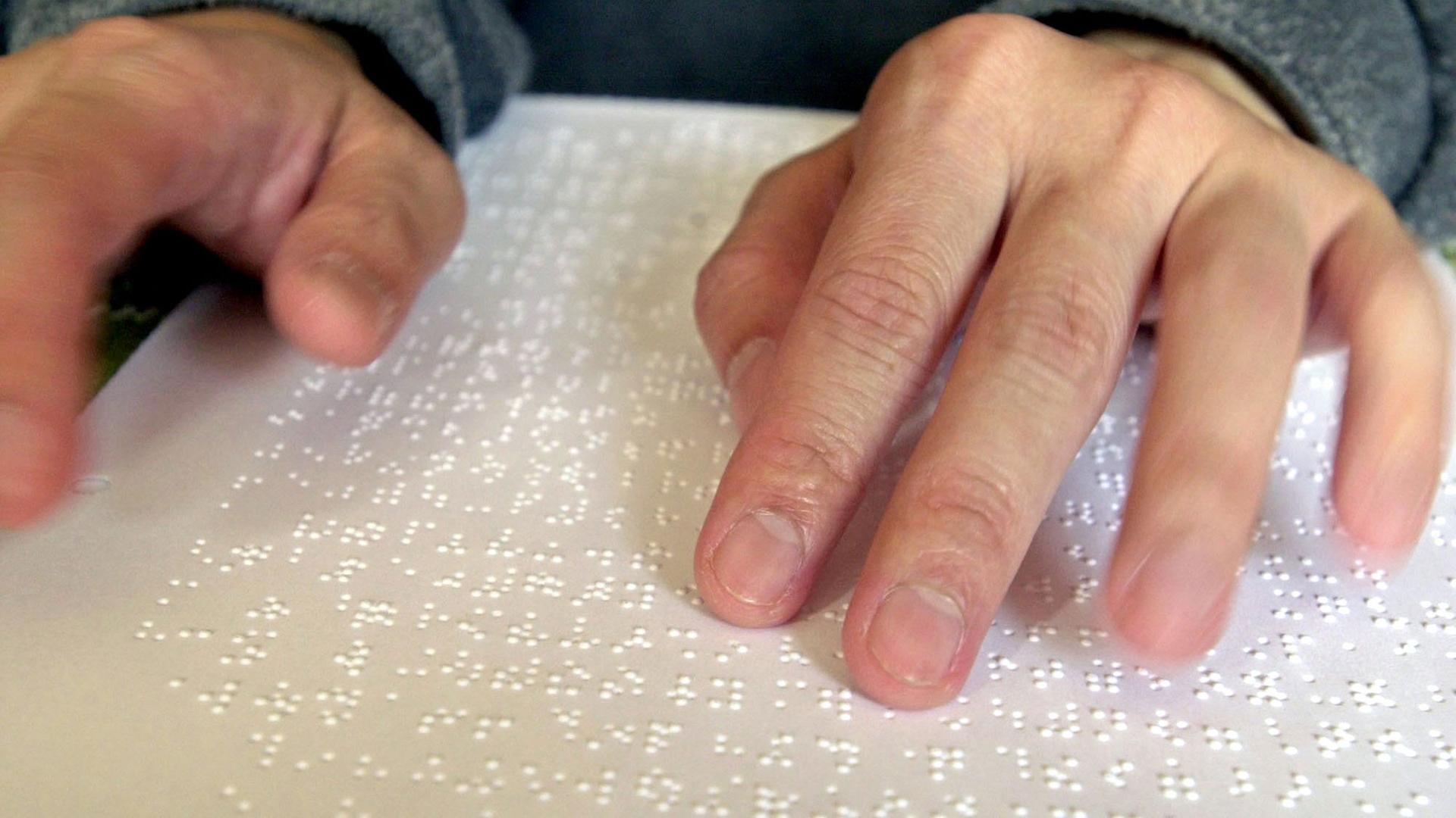 Ein Blinder liest mit seinen Händen Braille-Schrift, die Blindenschrift.