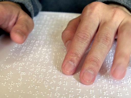 Ein Blinder liest mit seinen Händen Braille-Schrift, die Blindenschrift.