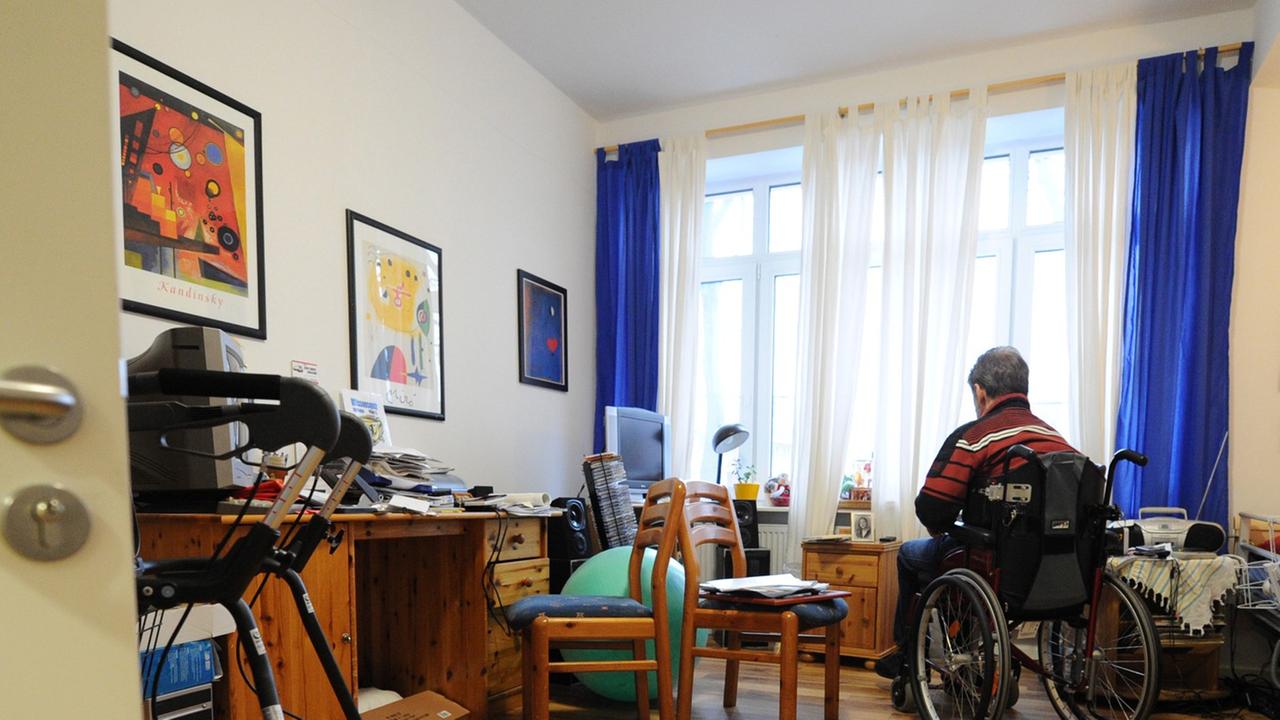 Ein Mann im Rollstuhl schaut in seinem Zimmer aus dem Fenster Ein Mann im Rollstuhl schaut in seinem Zimmer aus dem Fenster
